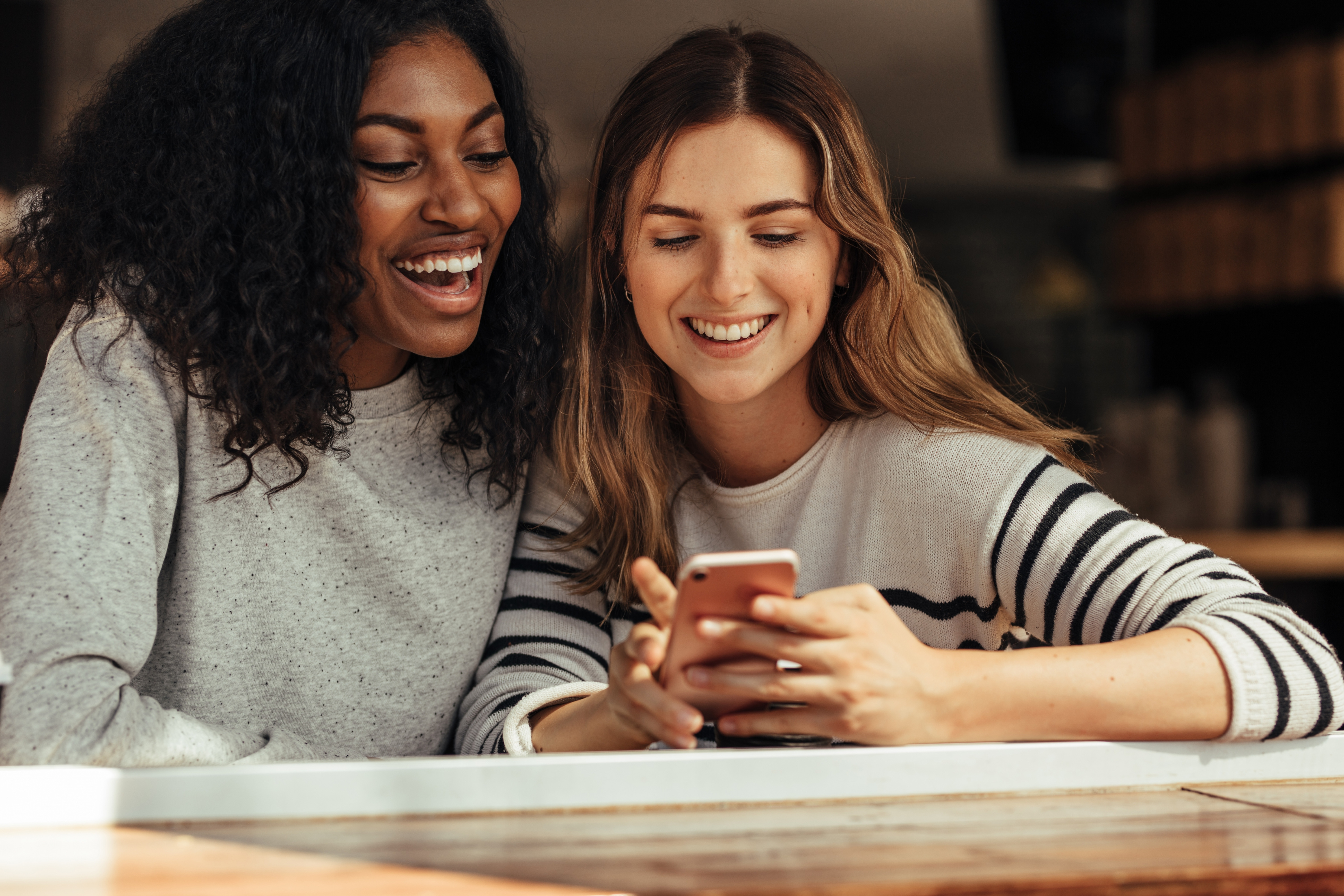 Photo de deux jeunes filles dont l'une d'entre elle qui tient un téléphone portable à la main, les deux femmes ont un grand sourire.