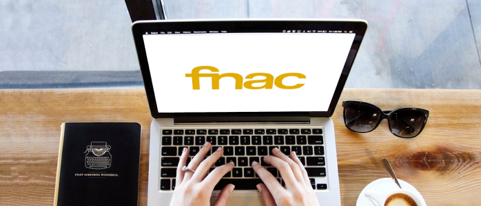 Une personne tape sur un ordinateur sur lequel le logo de la FNAC apparait